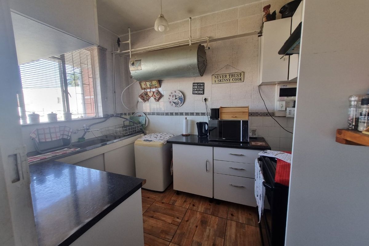 A functional kitchen featuring built-in cabinetry, laminate countertops, a stainless steel sink, and tiled finishes, with exposed plumbing and water heater infrastructure.