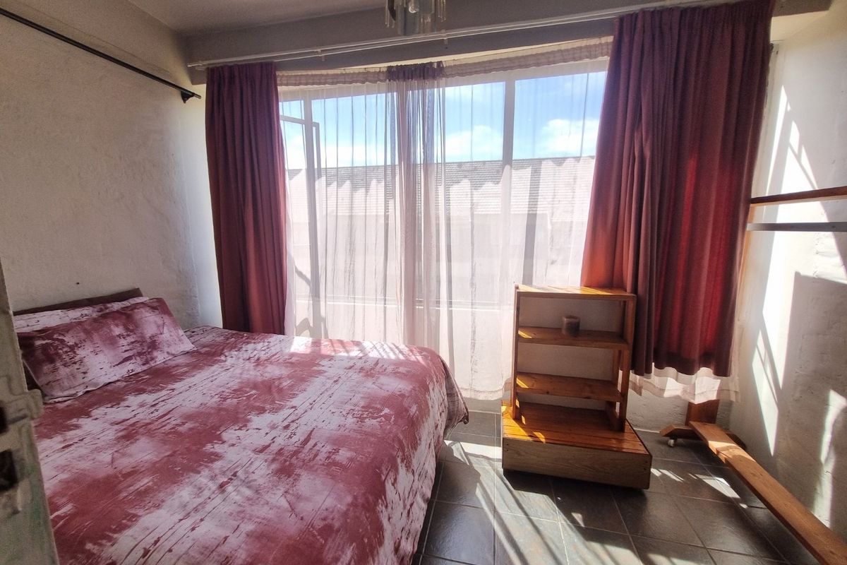 A bedroom featuring tiled flooring and a large window with curtain tracks, providing natural light.