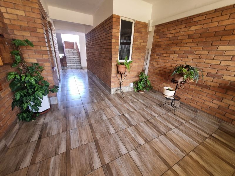 A well-maintained apartment hallway featuring exposed brick walls and modern wood-look tiled flooring, leading to a staircase.