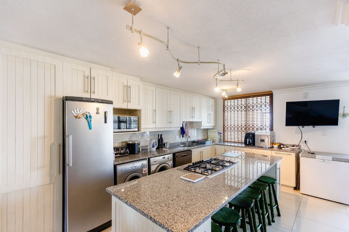 A functional kitchen featuring granite countertops, a central island with a gas hob, ample built-in cabinetry, and tiled flooring.
