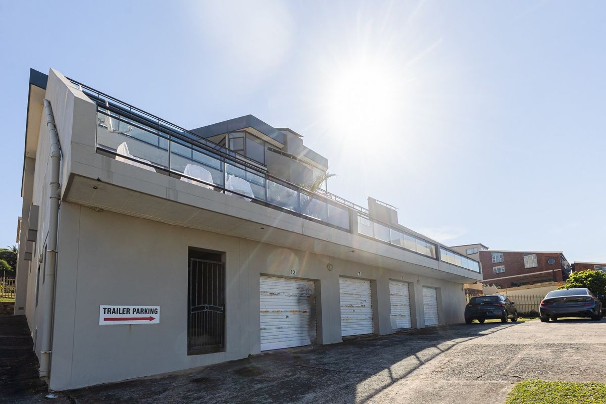 Exterior view of the apartment building featuring multiple ground-level roller garage doors and an upper-level balcony with glass balustrades.