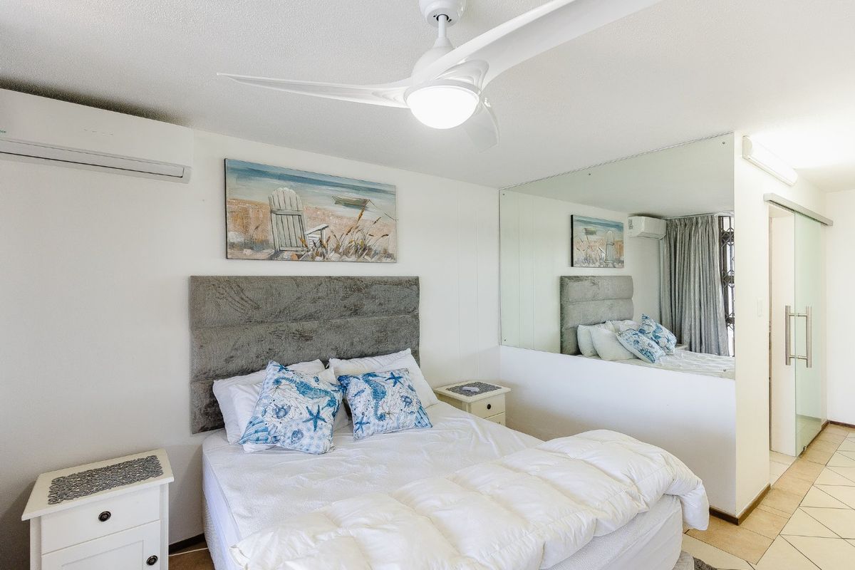 A well-maintained bedroom featuring a ceiling fan, split-system air conditioning, tiled flooring, and a large mirrored wall.