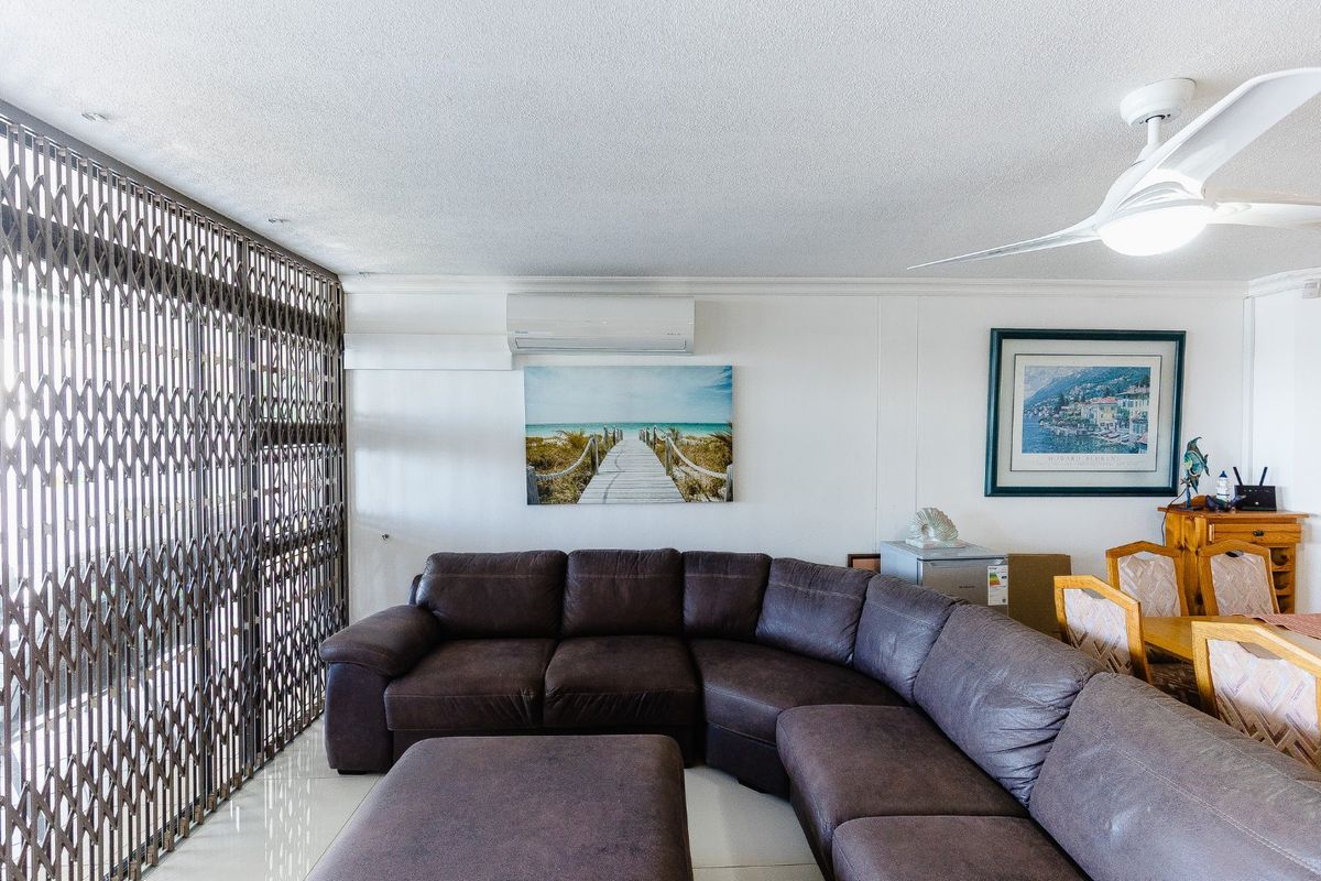 A living area featuring tiled flooring, a ceiling fan, and a wall-mounted split-system air conditioner, with a security gate leading to the balcony.