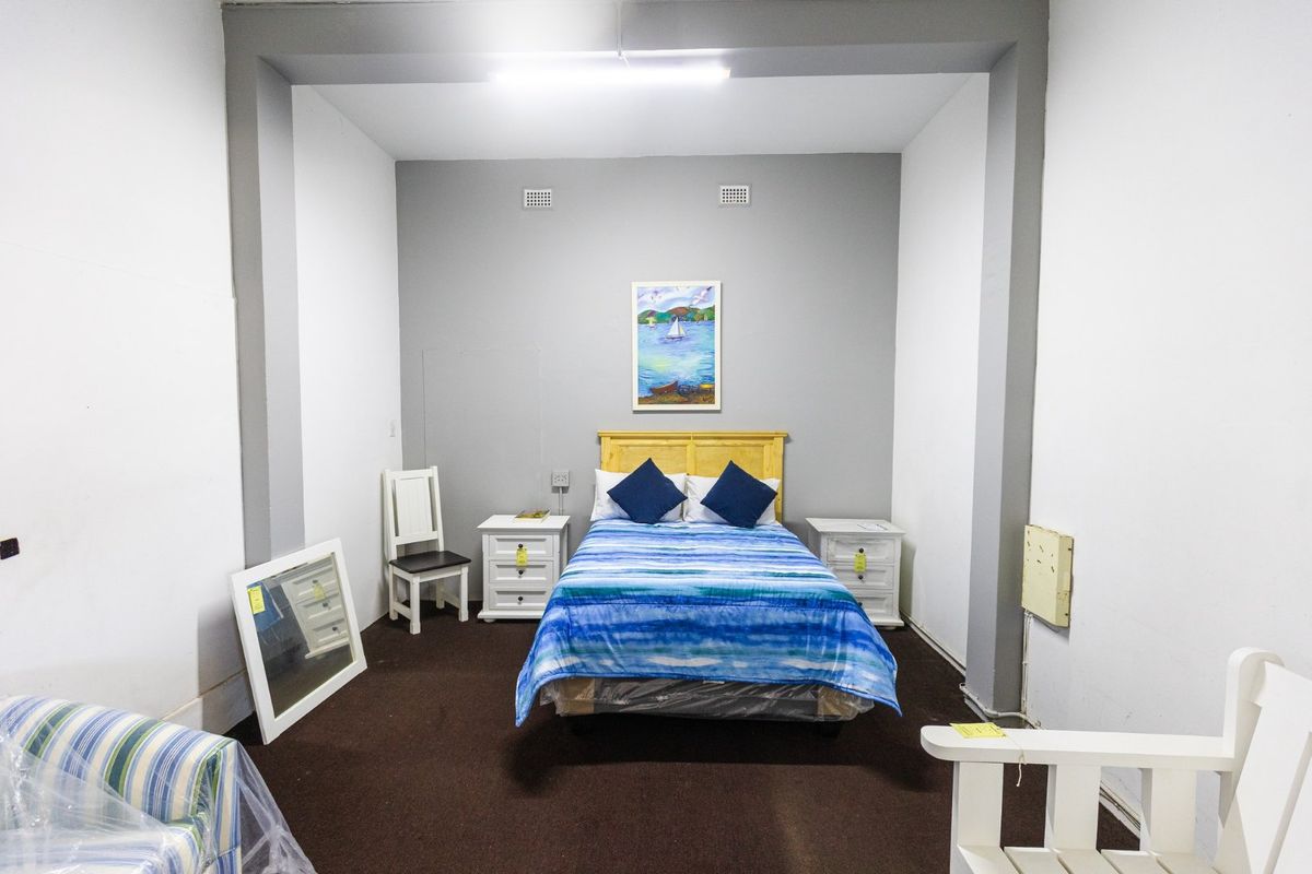 A simple bedroom space featuring dark carpeting, neutral grey walls, and basic overhead lighting, suitable for a functional sleeping area.
