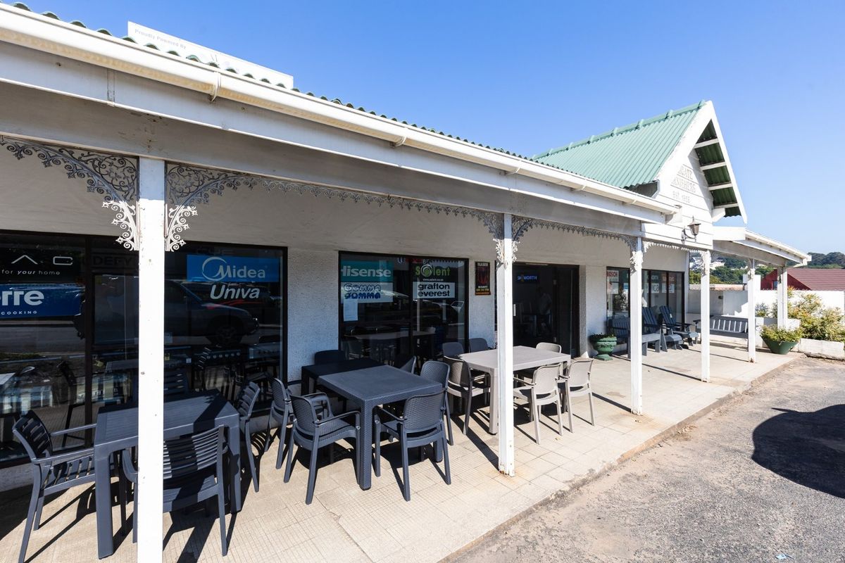 Commercial storefront featuring a covered veranda with decorative wrought iron detailing, tiled flooring, and large glass display windows under a metal roof.