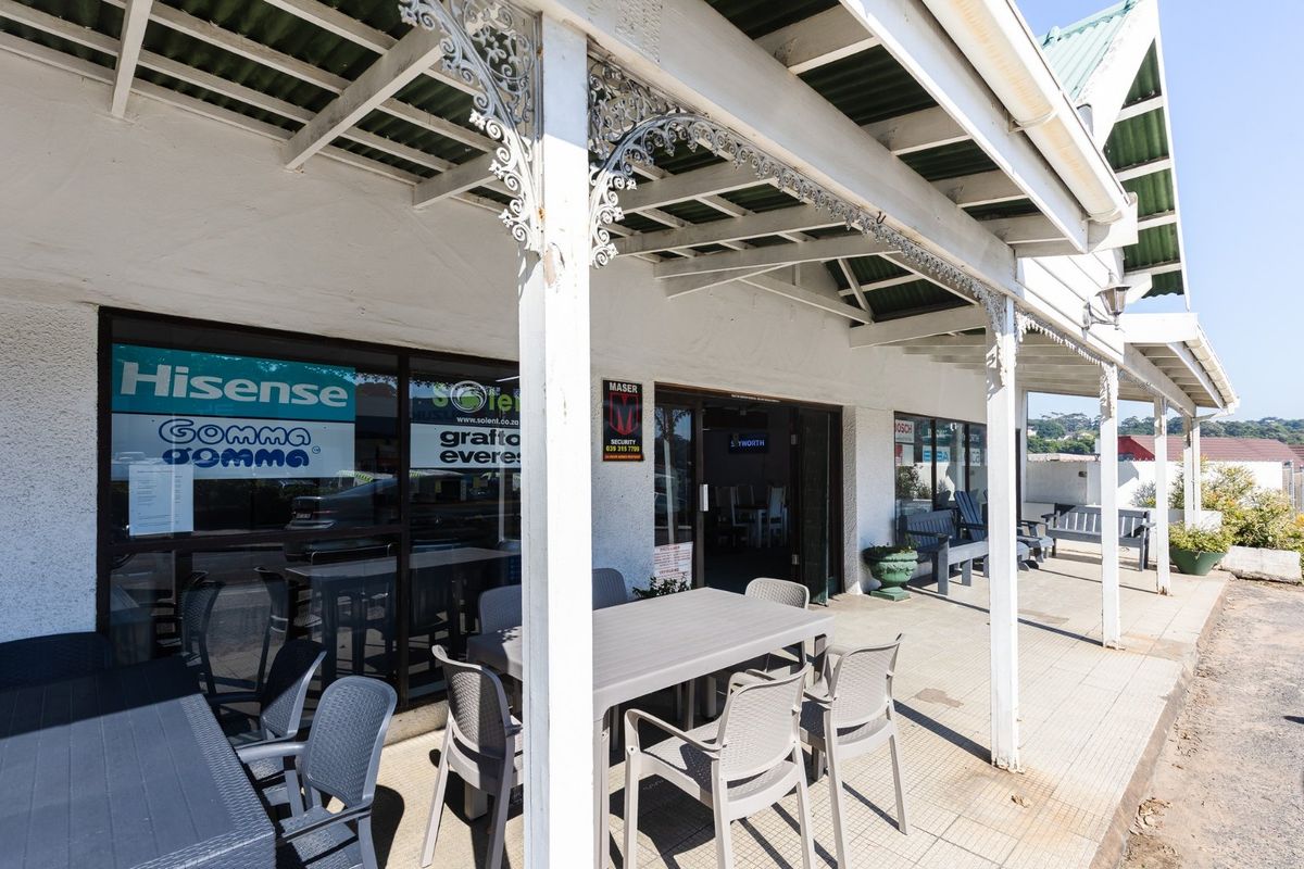 A covered commercial veranda featuring decorative ironwork, tiled flooring, and large glass storefront windows, providing an accessible entrance to the property.