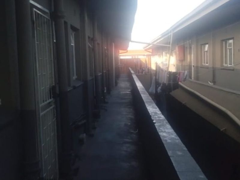 An exterior apartment walkway or balcony area featuring a concrete balustrade and security gates, showing signs of wear.