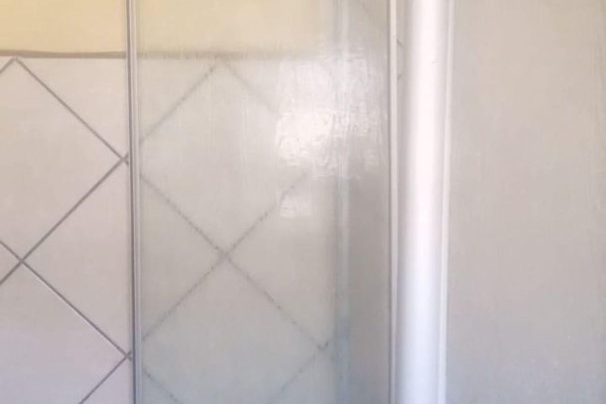 A bathroom shower area featuring a framed glass enclosure and diamond-patterned wall tiles, requiring cosmetic updates to improve the overall aesthetic.