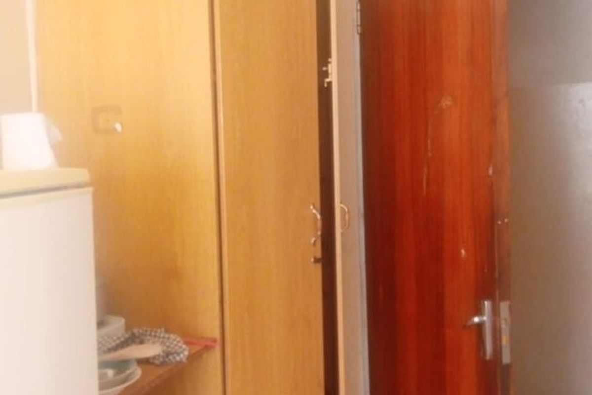 A small kitchen area featuring built-in wooden cabinetry and tiled flooring, currently showing signs of wear and dated finishes.