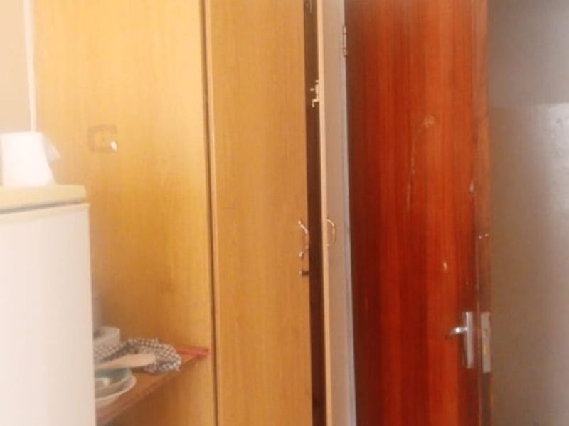 A small kitchen area featuring built-in wooden cabinetry and tiled flooring, currently showing signs of wear and dated finishes.