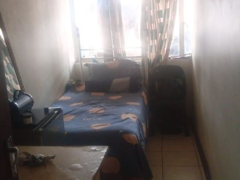 A compact bedroom featuring tiled flooring and a window with security bars, requiring cosmetic updates to improve the overall aesthetic and brightness.
