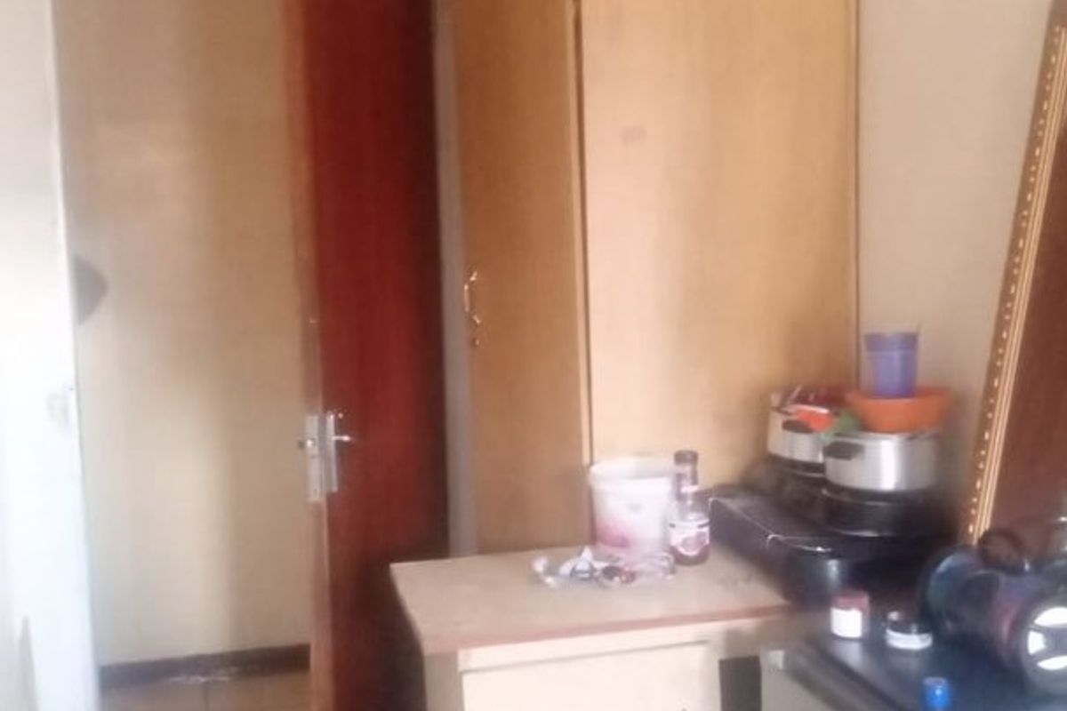 A bedroom featuring tiled flooring, a built-in cupboard, and coved ceiling detailing, showing signs of wear and ceiling staining.