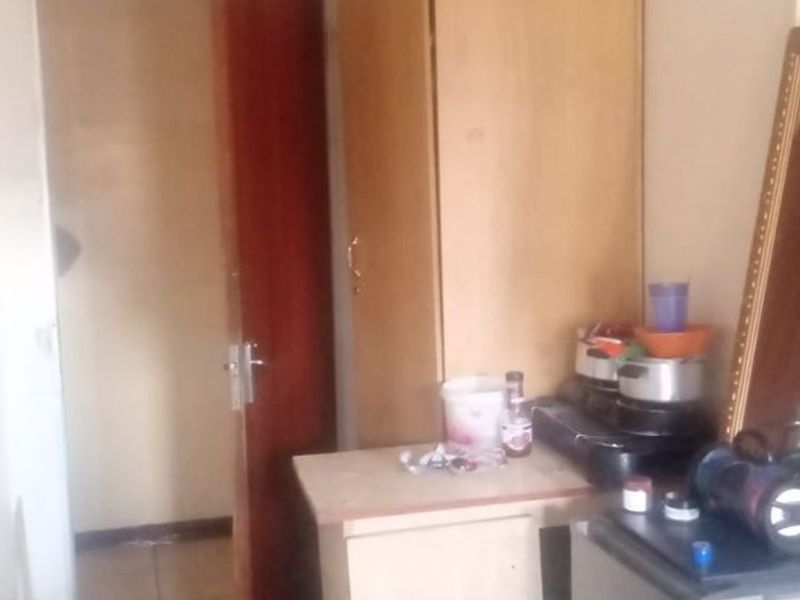 A bedroom featuring tiled flooring, a built-in cupboard, and coved ceiling detailing, showing signs of wear and ceiling staining.