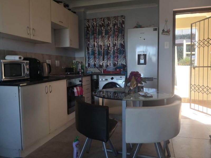 Open-plan kitchen and dining area featuring built-in cabinetry, tiled flooring, and direct access to an outdoor patio through a security gate.