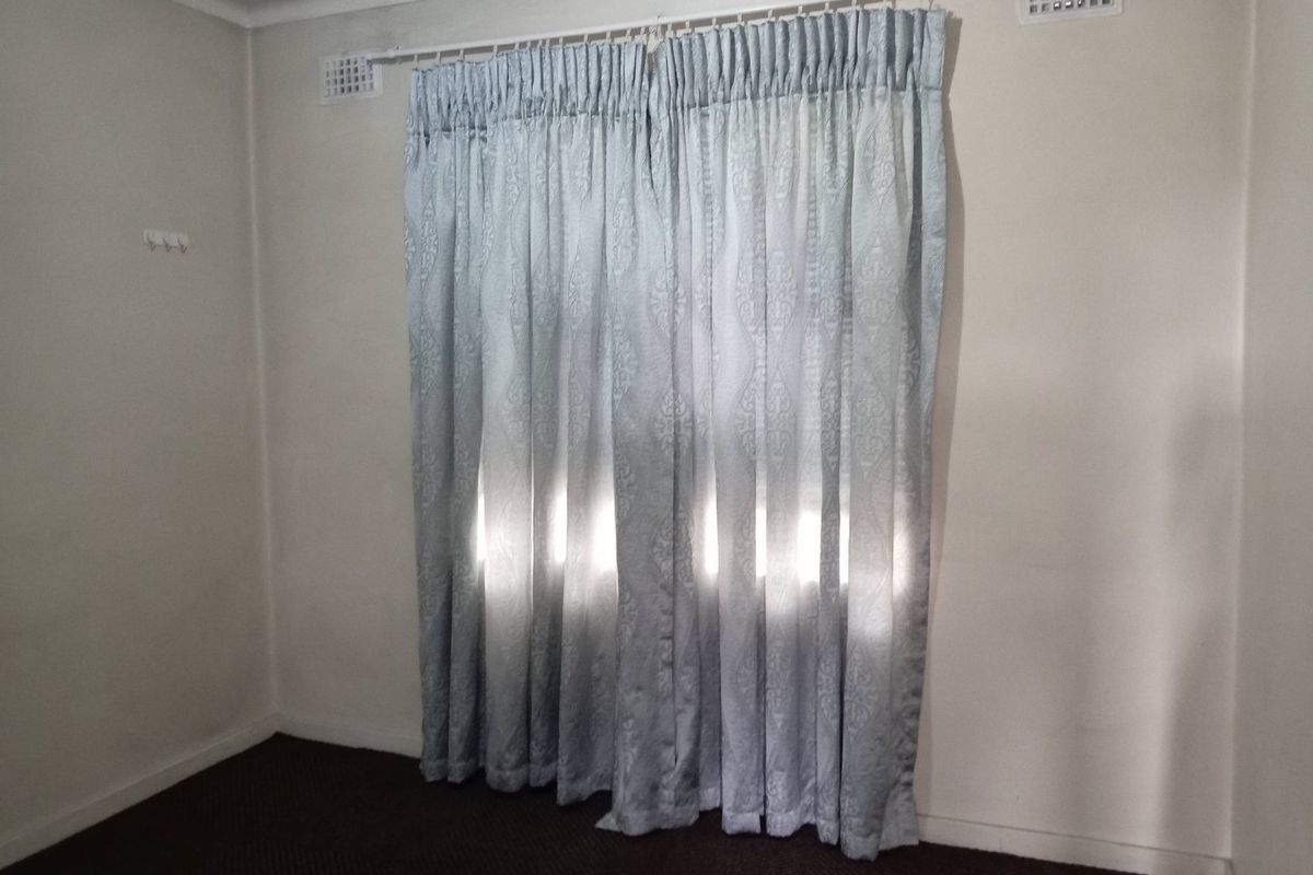 A simple bedroom space featuring neutral walls, carpet flooring, and installed curtain rods with ventilation grilles.