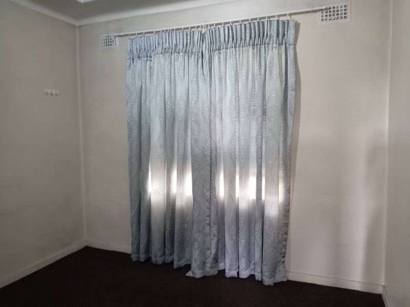 A simple bedroom space featuring neutral walls, carpet flooring, and installed curtain rods with ventilation grilles.