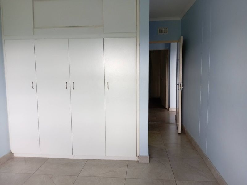 A clean, empty bedroom featuring built-in cupboards, neutral tiled flooring, and direct access to the hallway.