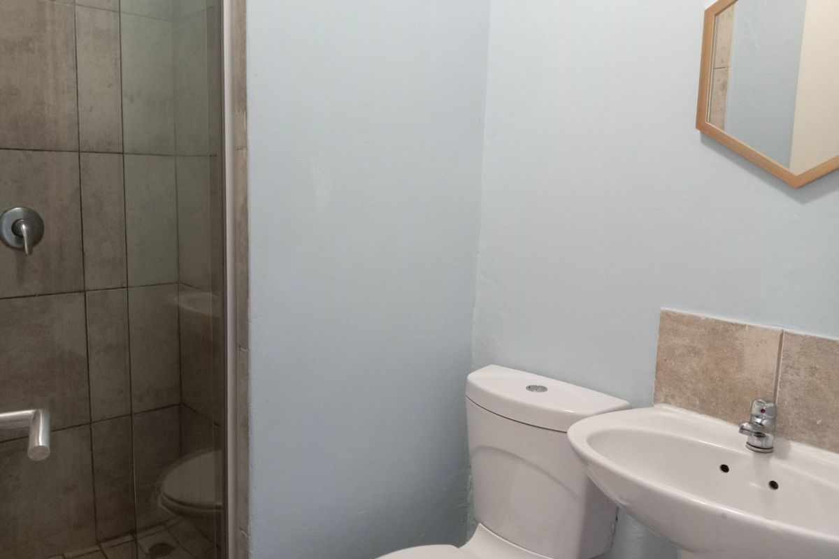 A functional bathroom featuring a glass-enclosed shower with tiled walls, a pedestal basin, and a standard toilet.