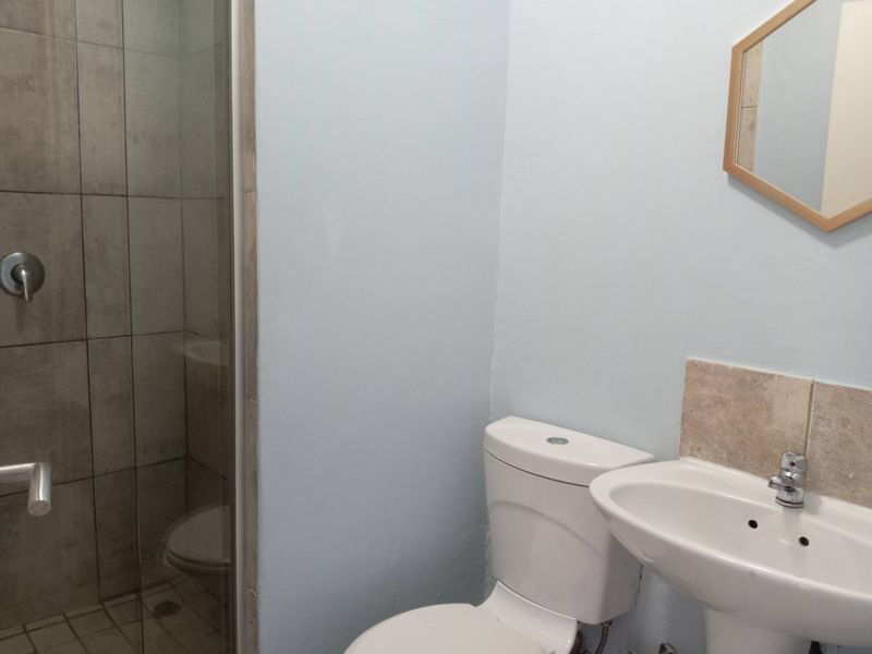 A functional bathroom featuring a glass-enclosed shower with tiled walls, a pedestal basin, and a standard toilet.