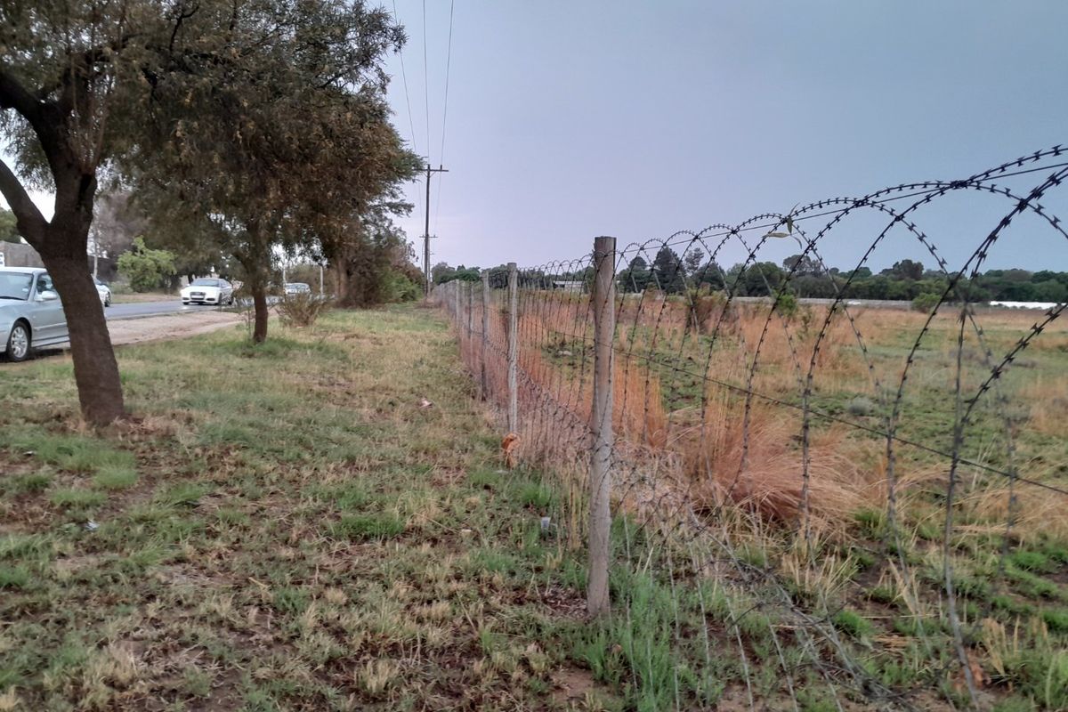 A view of the property boundary featuring a wire fence with barbed wire topping, adjacent to a public road and utility infrastructure.