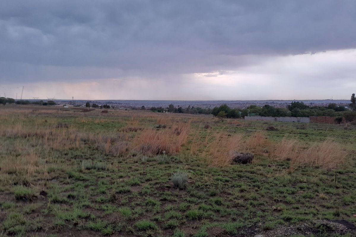 A wide-angle view of the vacant residential land, showcasing the natural landscape and surrounding area under a cloudy sky.