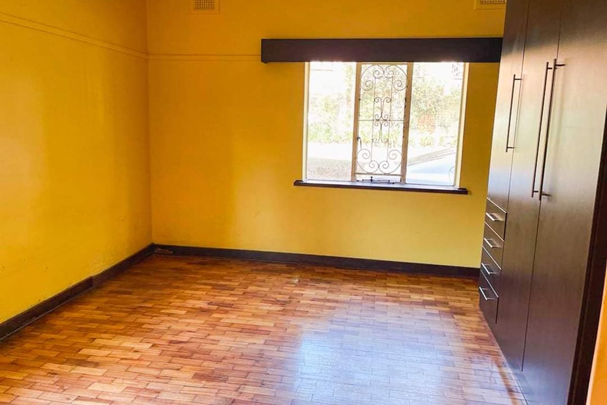 An empty bedroom featuring parquet flooring, a built-in wardrobe, and security bars on the window.