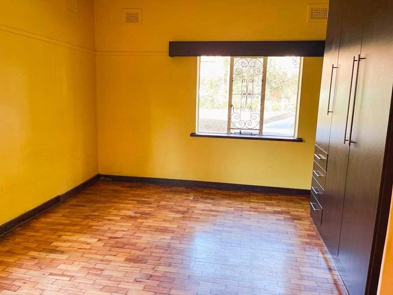 An empty bedroom featuring parquet flooring, a built-in wardrobe, and security bars on the window.