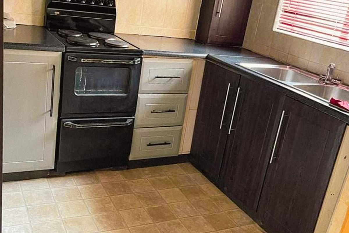 A functional kitchen featuring dark and light cabinetry, a stainless steel sink, and a freestanding electric stove with an extractor fan.