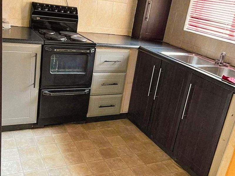 A functional kitchen featuring dark and light cabinetry, a stainless steel sink, and a freestanding electric stove with an extractor fan.