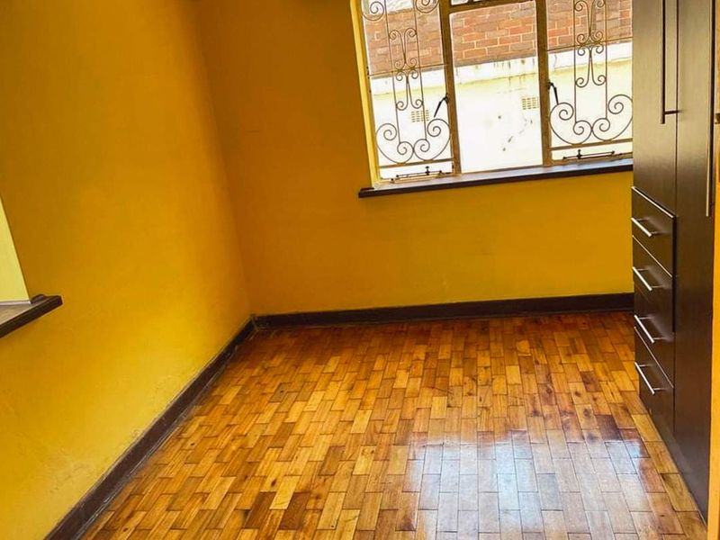 A vacant bedroom featuring original parquet flooring, a built-in wardrobe, and security burglar bars on the window.