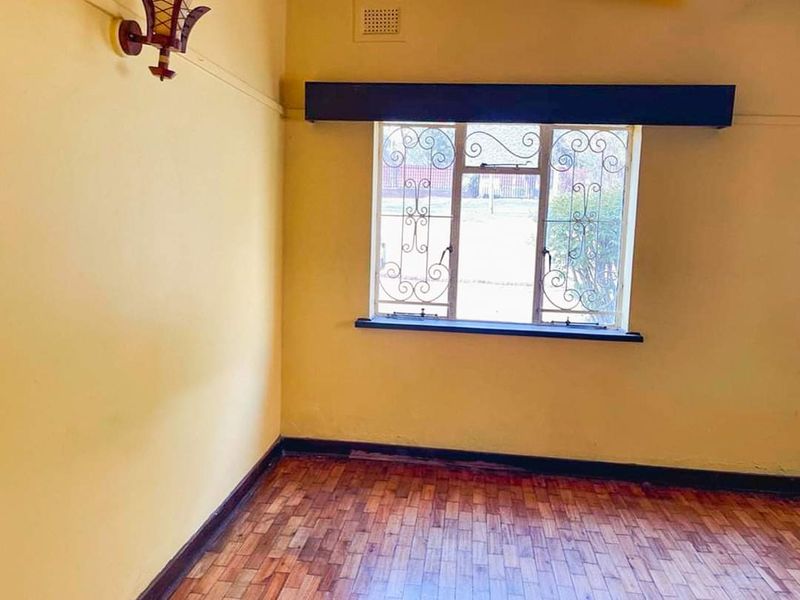 An empty bedroom featuring parquet flooring, security bars on the window, and neutral wall finishes.