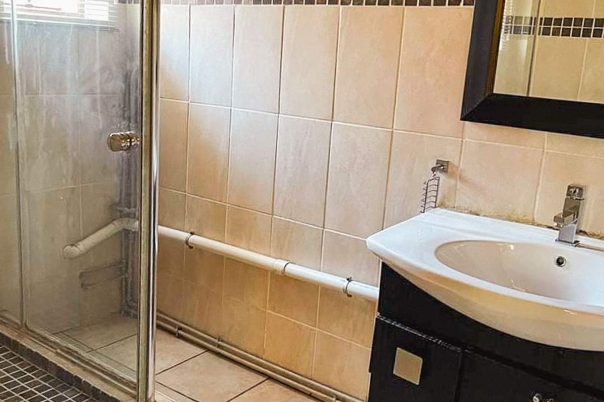 A functional bathroom featuring a shower enclosure, vanity cabinet with basin, and tiled finishes. The space would benefit from cosmetic updates and pipe concealment.
