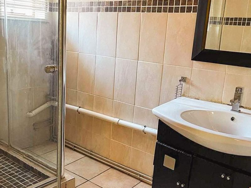A functional bathroom featuring a shower enclosure, vanity cabinet with basin, and tiled finishes. The space would benefit from cosmetic updates and pipe concealment.