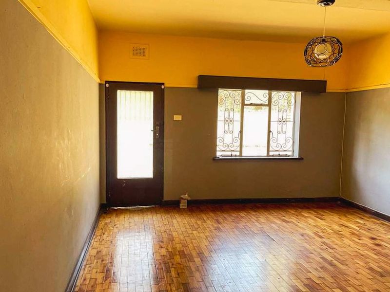 An empty living room featuring original parquet flooring, security bars on the windows, and a security door, offering a blank canvas for renovation.