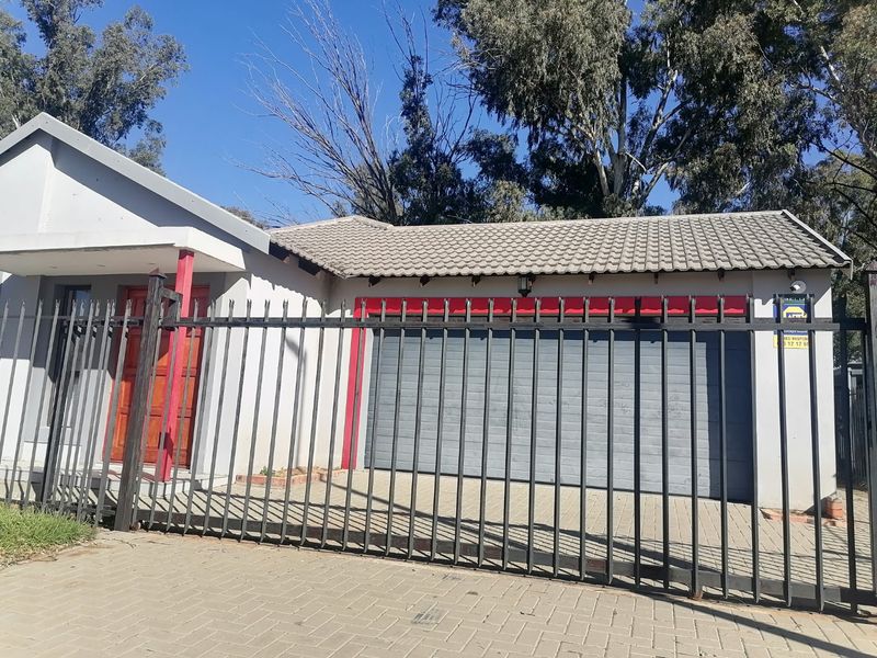 Front elevation of a residential property featuring a paved driveway, secure metal fencing, a single garage, and a timber entrance door.