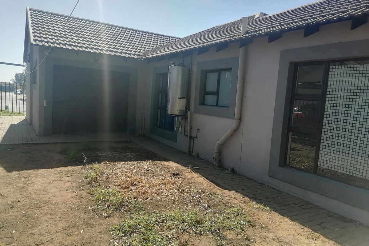 Rear exterior view of the property featuring a tiled roof, garage access, and an external geyser unit with a paved area and garden space.