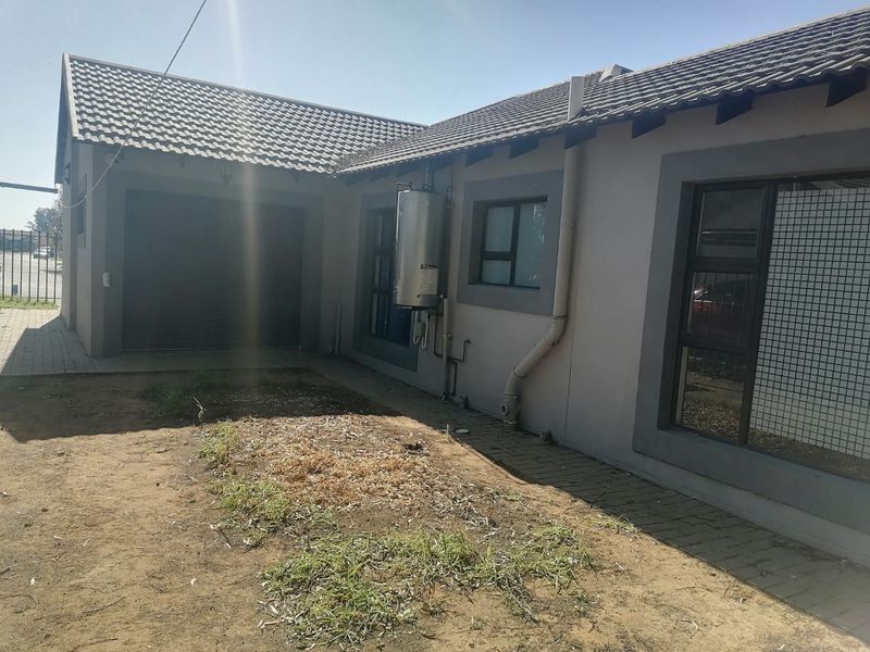 Rear exterior view of the property featuring a tiled roof, garage access, and an external geyser unit with a paved area and garden space.