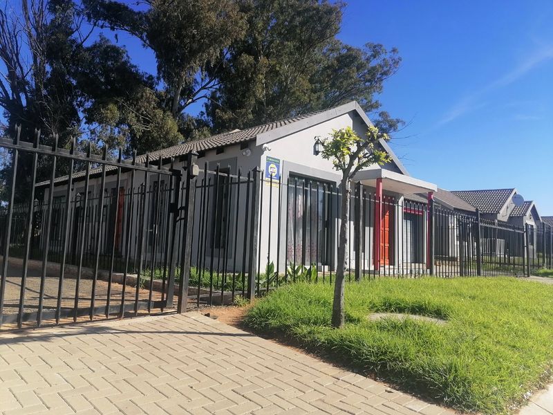 Front exterior view of a residential house featuring a paved driveway, secure metal fencing, and a tiled roof structure.