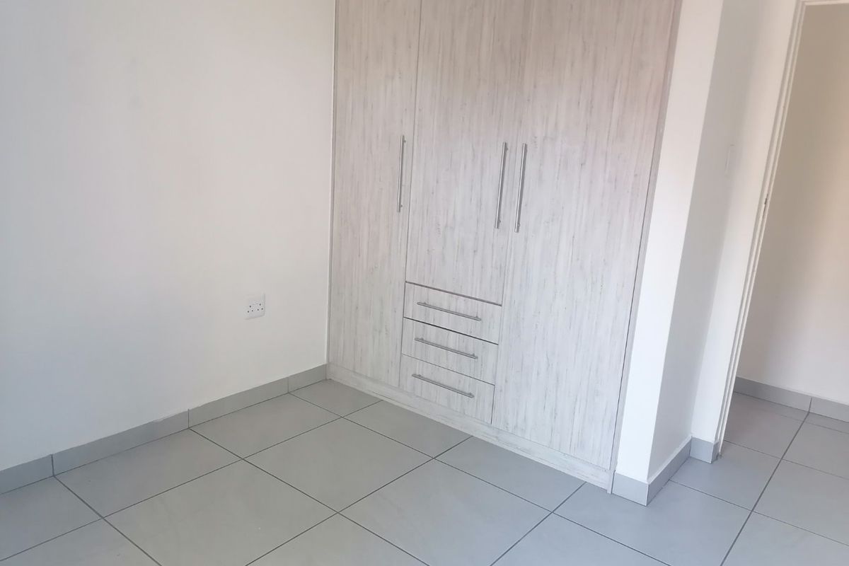 A clean, empty bedroom featuring neutral tiled flooring and modern built-in cupboards with integrated drawer storage.