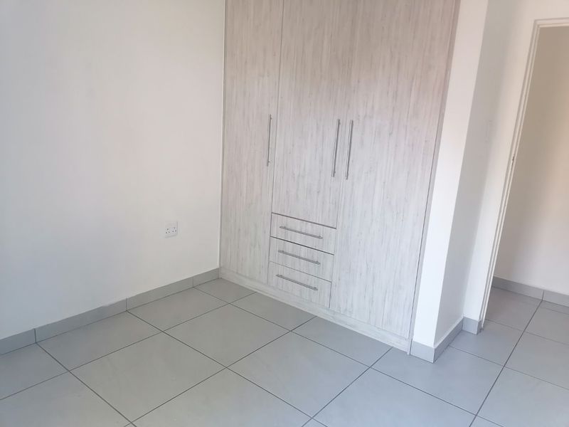 A clean, empty bedroom featuring neutral tiled flooring and modern built-in cupboards with integrated drawer storage.