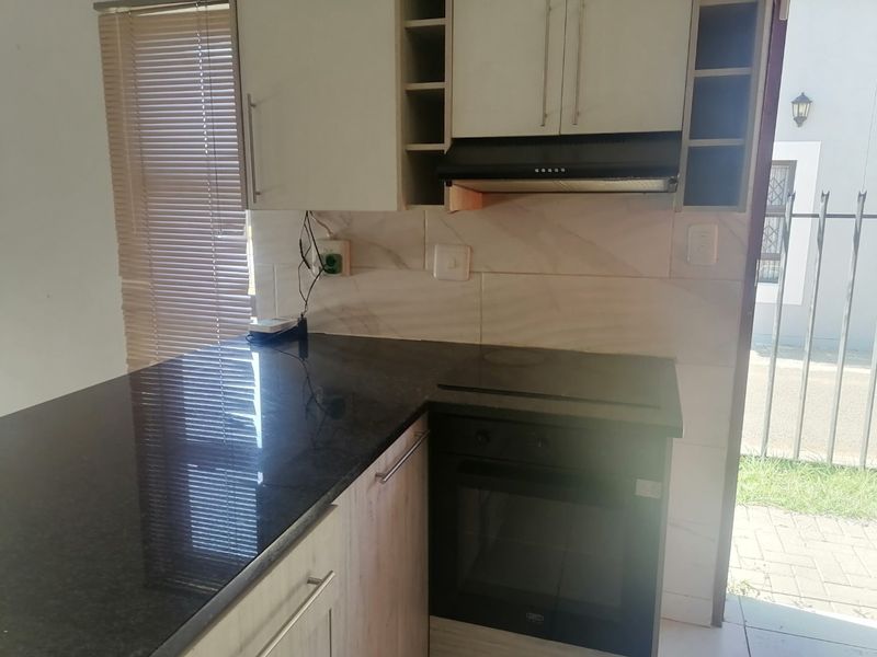 Compact kitchen featuring built-in cabinetry, granite countertops, integrated oven, hob, and extractor fan with a tiled backsplash.