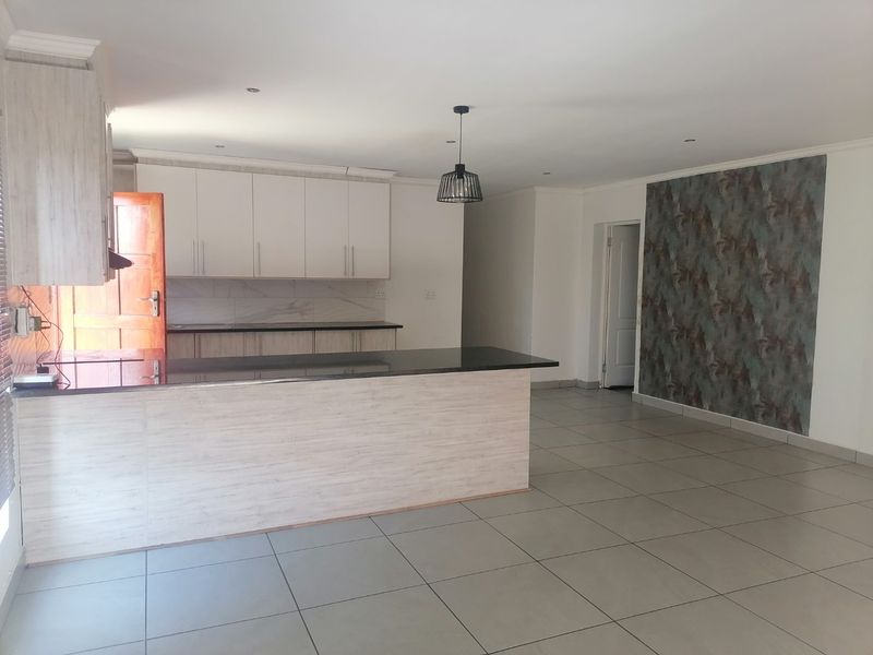 Spacious open-plan kitchen and living area featuring modern cabinetry, granite countertops, tiled flooring, and a decorative feature wall.
