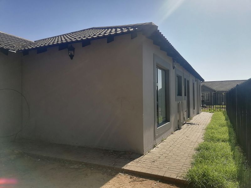 Rear exterior view of the property featuring a paved walkway, tiled roof, and aluminium window frames along the side elevation.