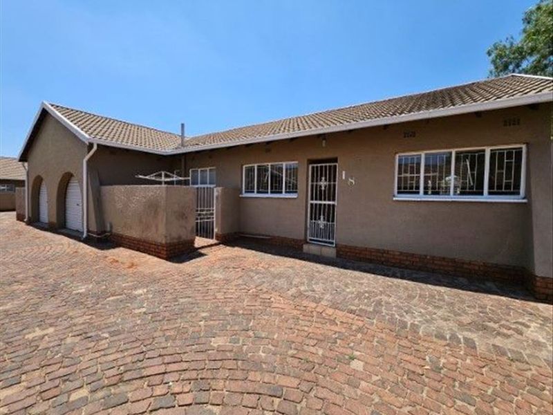 Front exterior view of a townhouse featuring a tiled roof, plastered walls, brick paved driveway, and security gates with burglar bars.