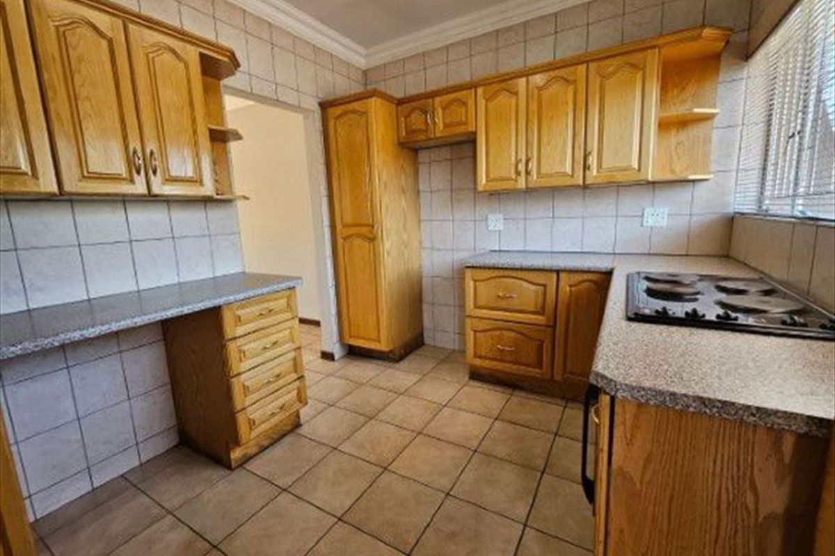 A functional kitchen featuring traditional wooden cabinetry, laminate countertops, tiled backsplash, and a built-in hob, offering a classic layout ready for modernization.
