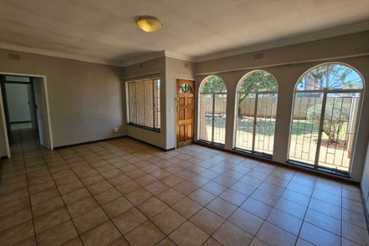Spacious living area featuring ceramic tiled flooring, coved ceilings, and large arched windows with security bars, offering a bright and open layout.