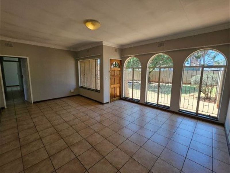 Spacious living area featuring ceramic tiled flooring, coved ceilings, and large arched windows with security bars, offering a bright and open layout.