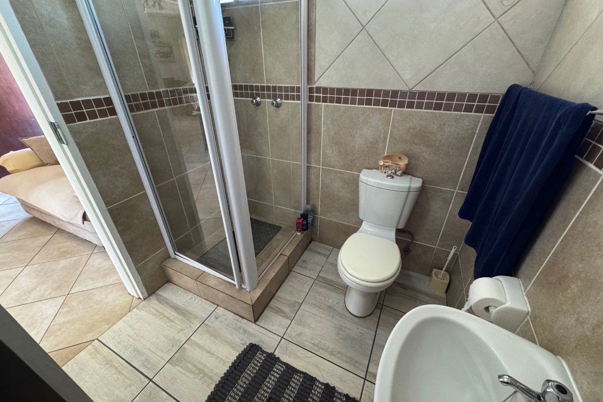 A functional bathroom featuring a glass-enclosed shower, a standard toilet, and a pedestal basin with neutral wall and floor tiling.