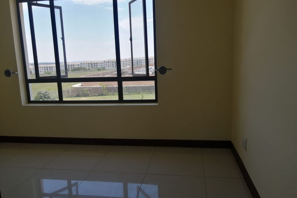 A bright, empty bedroom featuring large casement windows with a view, neutral walls, and clean tiled flooring.