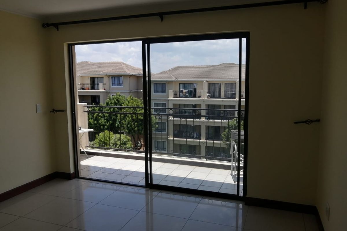 An empty living room featuring tiled flooring and a large sliding glass door that opens onto a private balcony with neighborhood views.